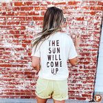 A cream short sleeve tee with a big sun face on the front in brown and grey with 'The Sun will come up' written on the backside in brown