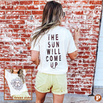 A cream short sleeve tee with a big sun face on the front in brown and grey with 'The Sun will come up' written on the backside in brown